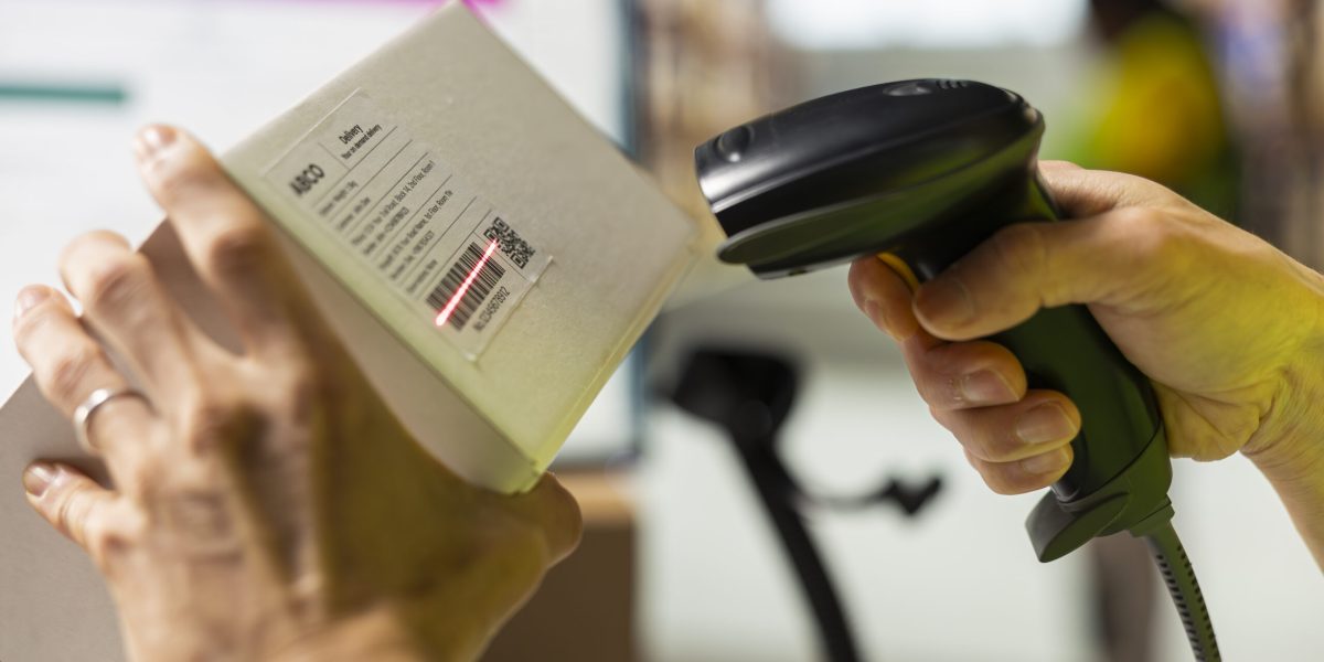 Close up of worker manages cargo barcode scanning in a distribution hub, preparing the goods with packaging, tagging and inventory checking. Man using a scanner in fulfillment center.