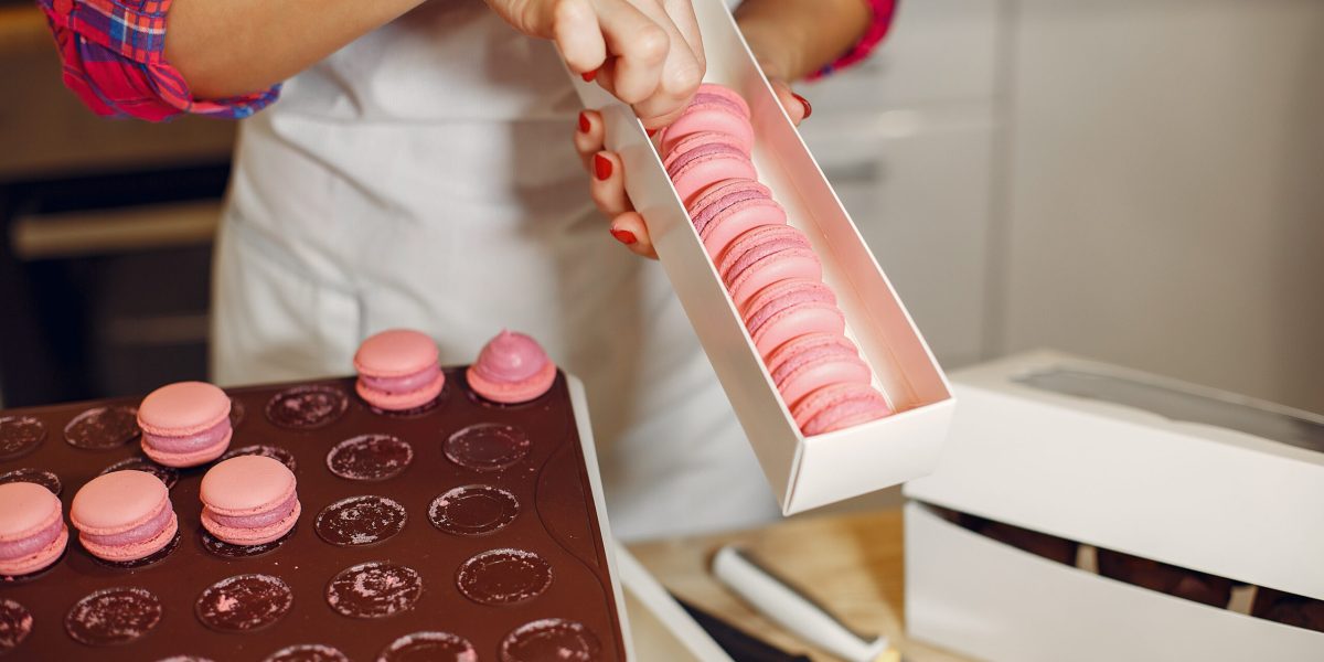 Confectioner in a kitchen. Woman in a uniform. Professional decorates the macaroni.