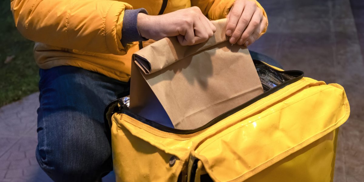 Delivery man in yellow jacket opening yellow backpack and taking a bag with order