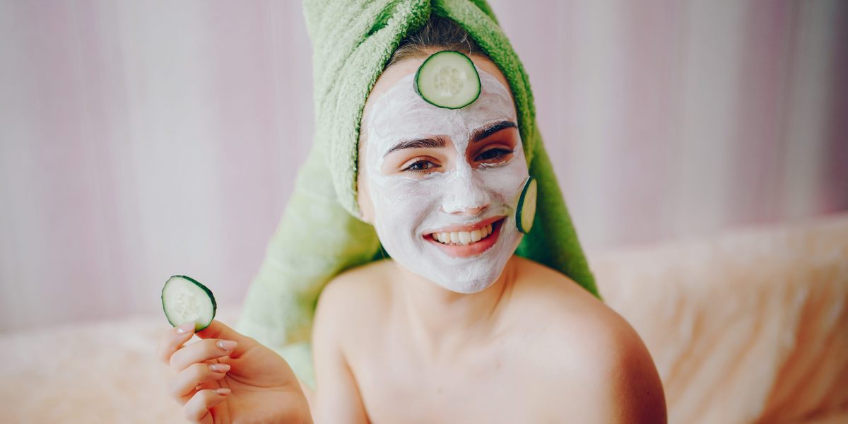 Beautiful girl sitting on the couch in the room. Lady in a green towel and with cucumber on her face