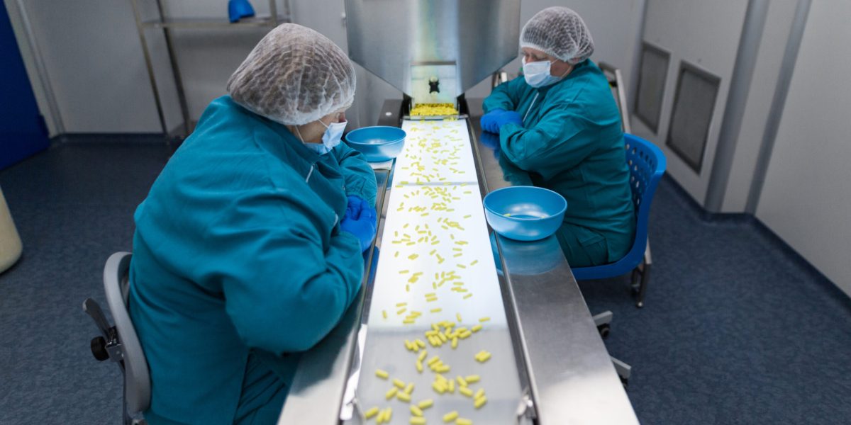 clean room, two women in blue lab suits work on line with pills