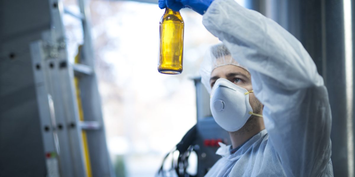 Technologist expert in beer production factory holding glass bottle and checking quality.