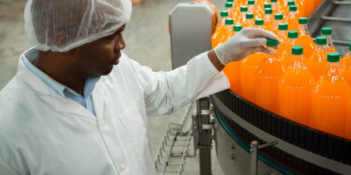 High angle view of serious male worker examining bottles in juice factory